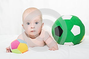 Baby boy or girl lying down on his belly and playing with soccer balls