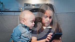 Baby boy and girl playing video games on smartphone on sofa