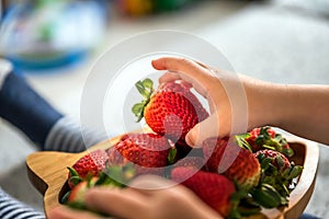 Baby boy hands touch and take raw fresh strawberries on wooden bamboo plate indoor. baby exploring fruit