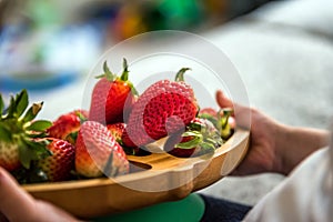 Baby boy hands touch and take raw fresh strawberries on wooden bamboo plate indoor. baby exploring fruit