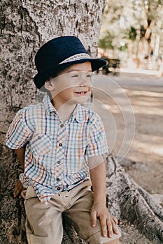 Baby boy in hat in the park sitting on a tree and smiling