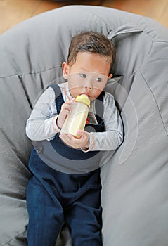 Baby boy holding and feeding milk from bottle lying on sofa