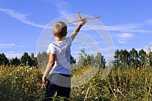 A baby boy is launching a toy airframe glider in a field against a blue sky background with clouds