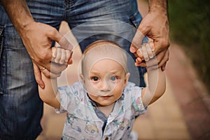 Baby boy learning to walk and making his first steps holding hands of father.