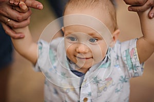 Baby boy learning to walk and making his first steps holding hands of father.