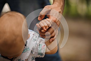 Baby boy learning to walk and making his first steps holding hands of father.