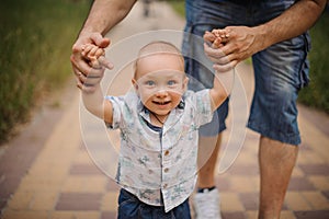 Baby boy learning to walk and making his first steps holding hands of father.