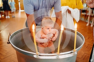 the baby boy is lowered into a font with holy water at baptism in the church.