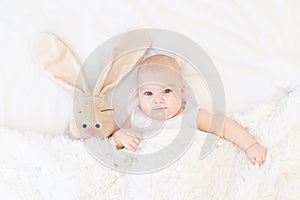 Baby boy lying or waking up in a crib with a bunny toy, cute, funny six-month-old, smiling little baby