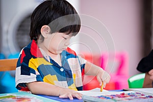 Baby boy is making art painting with crayons. Preschoolers are learning at home school. Empty space to enter text.