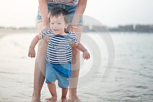 Baby boy making his first steps on the beach with his mother