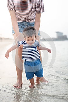 Baby boy making his first steps on the beach with his mother