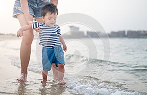 Baby boy making his first steps on the beach with his mother