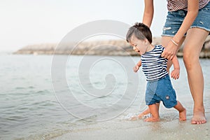 Baby boy making his first steps on the beach with his mother