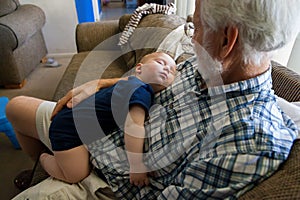 Baby Boy in a Onsie Passed Out Asleep on the Chest of his Grandfather Who is Looking at his Grandson