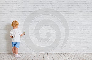 Baby boy with paint brush standing back near brick wall photo