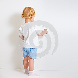 Baby boy with paint brush rear view standing near blank wall