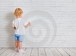 Baby boy with paint brush standing back near brick wall