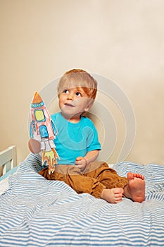 Baby boy play with paper rocket sitting on the bed