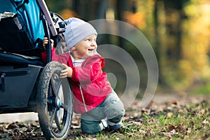 Baby boy playing in autumn forest with stroller, outdoors fun