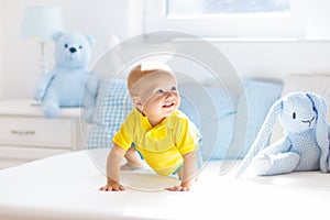 Baby boy playing on bed in sunny nursery