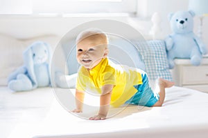 Baby boy playing on bed in sunny nursery