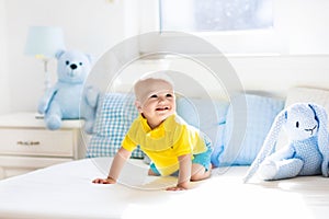 Baby boy playing on bed in sunny nursery