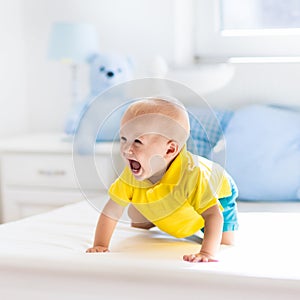 Baby boy playing on bed in sunny nursery