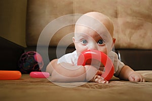 Baby boy playing with developing toy lying on sofa. Early baby development concept.