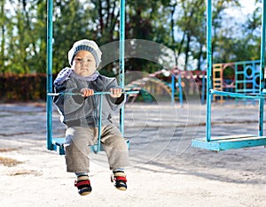 Baby boy playing on swing in autumn park