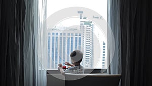 Baby boy playing a toy nearing the window in bedroom of high building in bangkok Thailand