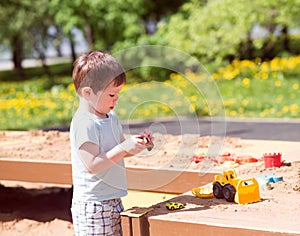 A baby boy plays with toys, cars in the sand on the playground. Kindergarten