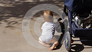 Baby boy plays with the wheel of a stroller, rocking it back and forth
