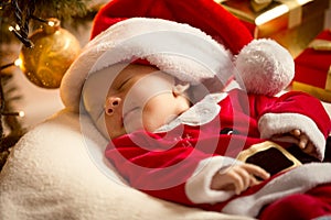 Baby boy in Santa costume lying under Christmas tree. Christmas