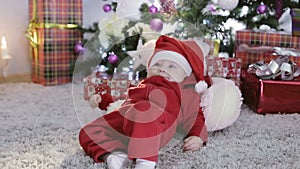 Baby boy in Santa costume sitting under the Christmas tree and falls.