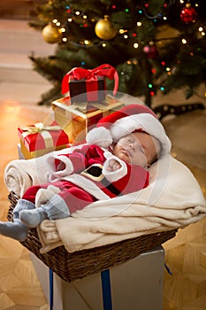 Baby boy in Santa costume sleeping under Christmas tree