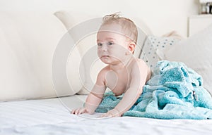 Baby boy after shower covered in blue blanket on sofa at living