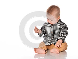 Baby boy sits and examines his hands on a white background.