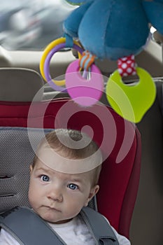 Baby boy sitting in child car seat with rattle hanging from ceiling