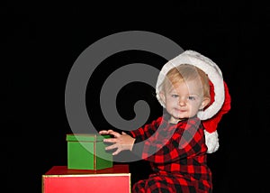 Baby boy sitting with Christmas presents wearing Santa Hat looking at viewer