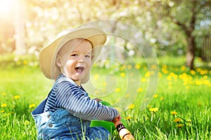 Baby boy sitting on the grass with dandelion flowers in the garden