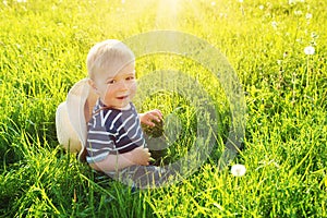 Baby boy sitting in grass on the fieald with dandelions