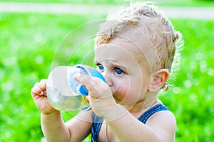 Baby boy sitting on the grass in a park and drinking from the bottle.