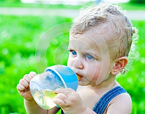 Baby boy sitting on the grass in a park and drinking from the bottle.