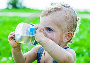 Baby boy sitting on the grass in a park and drinking from the bottle.