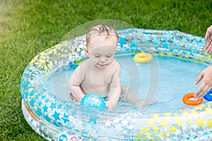 Cute baby boy sitting in inflatable swimming pool and playing with blue ball