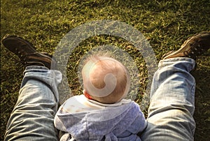 Baby boy sitting over grass between his fathers legs