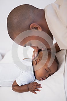 Baby boy sleeping peacefully on couch with father kissing head