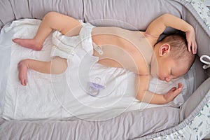 A baby boy sleeps in a cocoon on a cot. A newborn baby in a diaper is lying naked on the bed