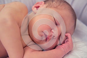 A baby boy sleeps in a cocoon on a cot. A newborn baby in a diaper is lying naked on the bed